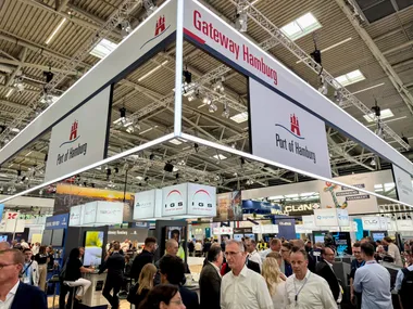 Messestand des Port of Hamburg auf der Transport Logistic in München. Im Vordergrund gehen Messebesucher entlang.